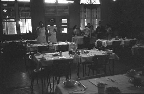 Eight people standing at back of set dining room.