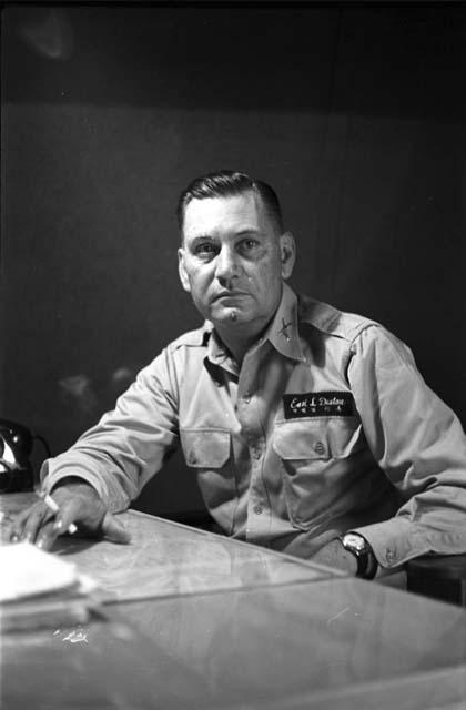 Military Man (Earl L. Denton name tag) sitting at desk, holding a cigarette.