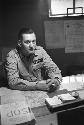 Military Man (Earl L. Denton name tag) sitting at desk, holding a cigarette.