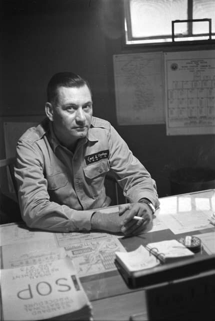 Military Man (Earl L. Denton name tag) sitting at desk, holding a cigarette.