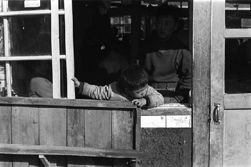 Child leaning out of wooden window frame.