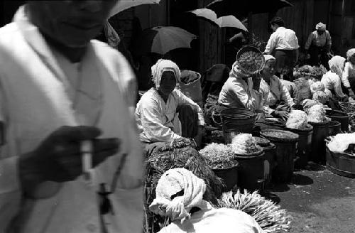 Women outdoors sitting with baskets of vegetables.