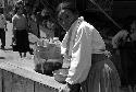 Woman pushing table/cart with some containers down a market street.