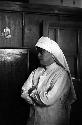 Nun with arms crossed, in front of wooden wall/furniture.