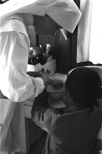 Nun treating child's hand over bowl.