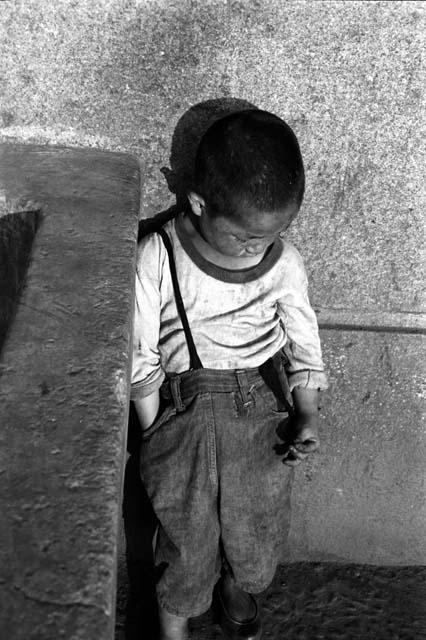 Boy standing against wall and looking down.