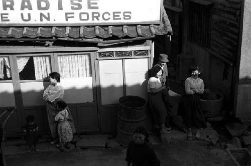 Few women, a child, and military men outside of a bar.