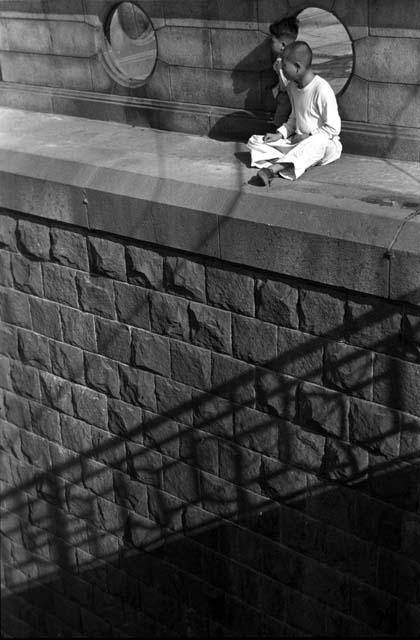 Two boys sitting on ledge on top of large stone wall.