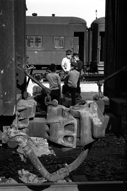 Boys standing beside a train; metal structure in foreground.