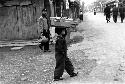 Child holding large metal pan on head, walking on street