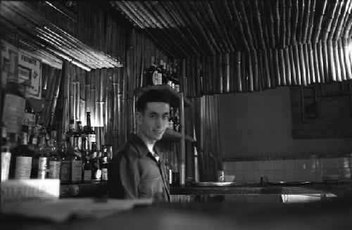 Military man standing in front of bar with liquor bottles.