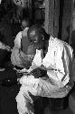 Old man in white clothes sitting and reading.