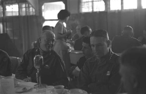 Military men sitting at table with a microphone on it, in Dining Hall.