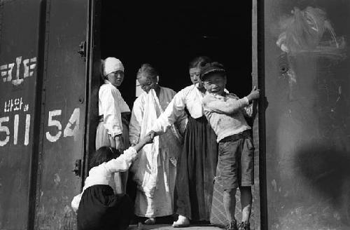 Women helping children climb onto train.