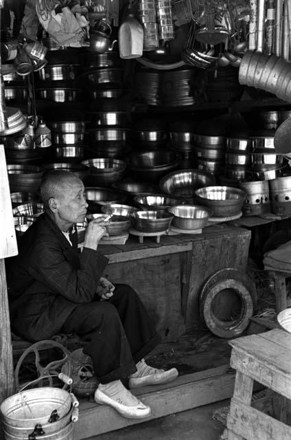 Man sitting in front of stand of pots.