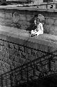 Two boys sitting on ledge on top of large stone wall.