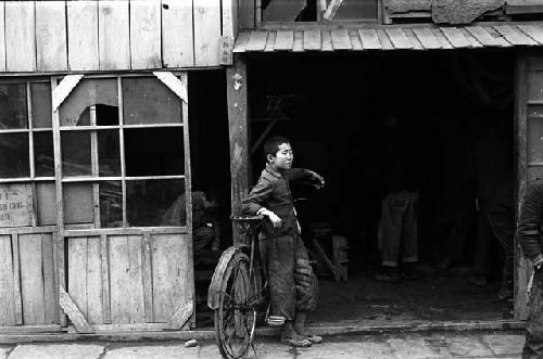 Young man leaning against bicycle under awning of building