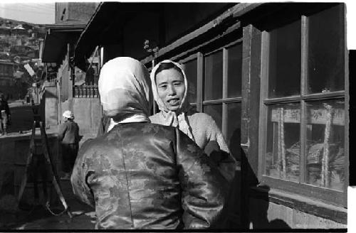 two women with shawls over their heads, speaking to each other