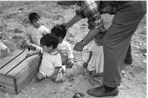 four small children sitting on the ground and a man standing over them