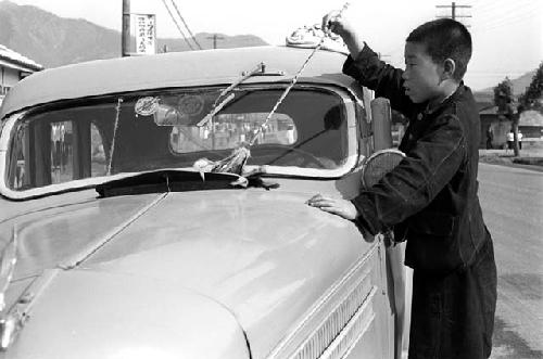 Boy dusting windshield of car with a broom