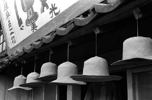 Hats hanging in a row from awning below a sign of a store.