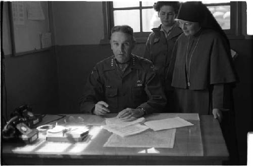 Man at a desk and a nun standing behind him