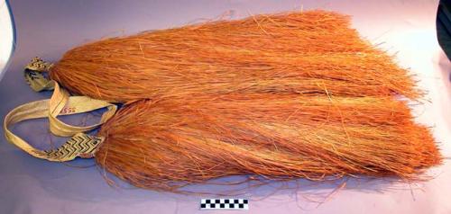 Two large tufts of fiber fringe connected with woven strap, buff, brown, black