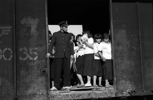 Girls in school uniforms in train car; uniformed conductor (?) also there.