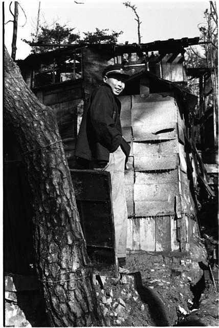 man with head turned and hat on, on a hill with house in background