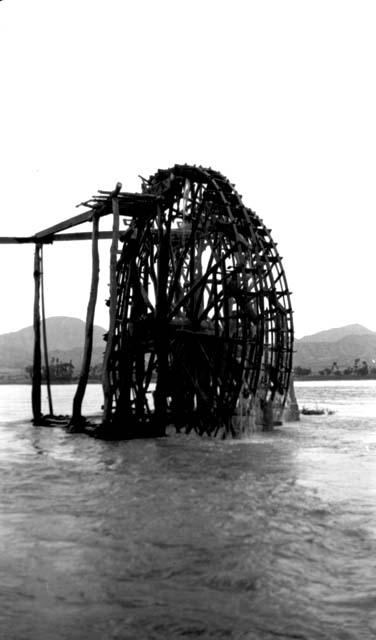 Waterwheel on river, hills in background