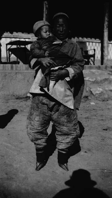 Woman with bound feet, holding baby; baby looking to the side