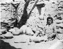 Hopi man sitting, with ceramic vessels next to him