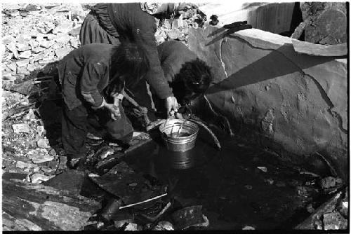 Women getting water with a bucket, a child on either side