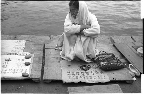 Woman with a sheet of paper spread before her and her back to a body of water