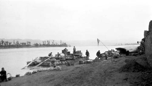 People preparing pontoon boat, supplies and American flag on shore