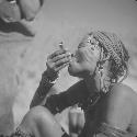 Woman wearing blue beads in her hair, smoking a pipe made from a cartridge