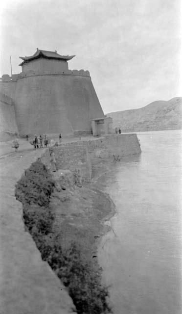 People walking near wall enclosing building on river