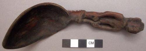 Wooden spoon, handle carved in human effigy: hands resting on flexed knee, no he