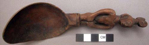 Wooden spoon, handle carved in human effigy: hands resting on flexed knee, hair