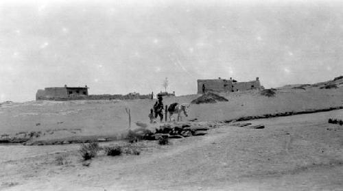 People and donkey approaching river, buildings in distance