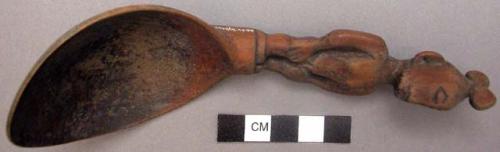 Wooden spoon, handle carved in human effigy: hands resting on flexed knees, fema