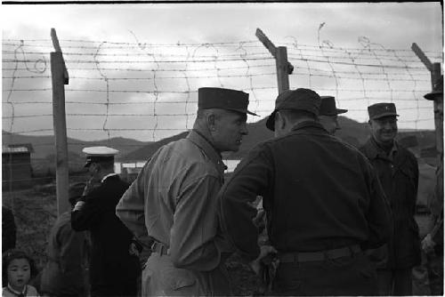 Military personnel standing next to a barbed wire fence