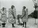 Three men displaying carved wooden plaques (shields?)