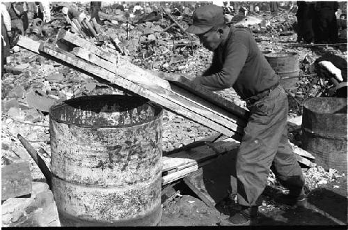 man holding a stack of wood planks propped up against a barrel