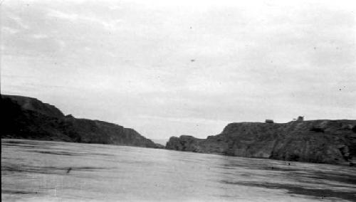 River flowing between cliffs, two buildings atop right cliff