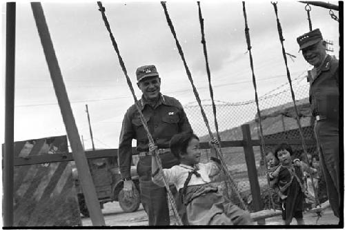 Men standing next to two small children on swings