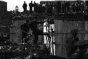 Crowd watching two people work on a fence