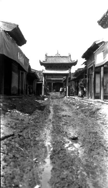 Muddy road to gateway, man carrying bundles