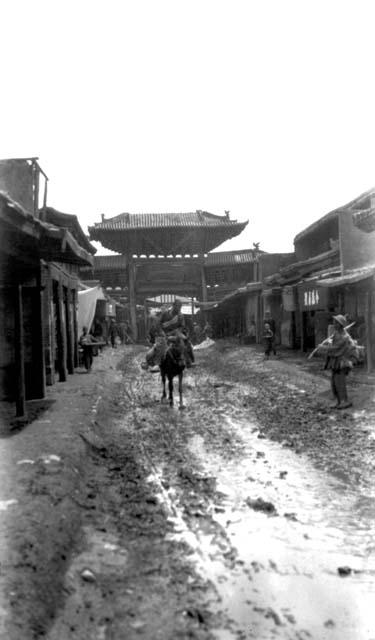 Person riding horse on muddy street, gateway behind