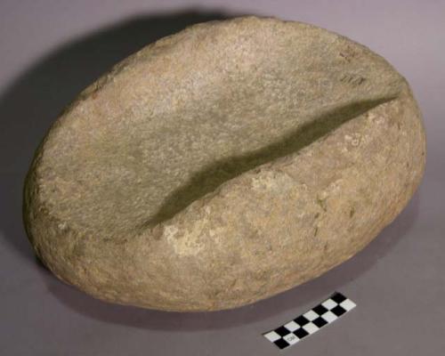 Metate. ovoid boulder. open-ended narrow trough metate. raised rim. ground quart